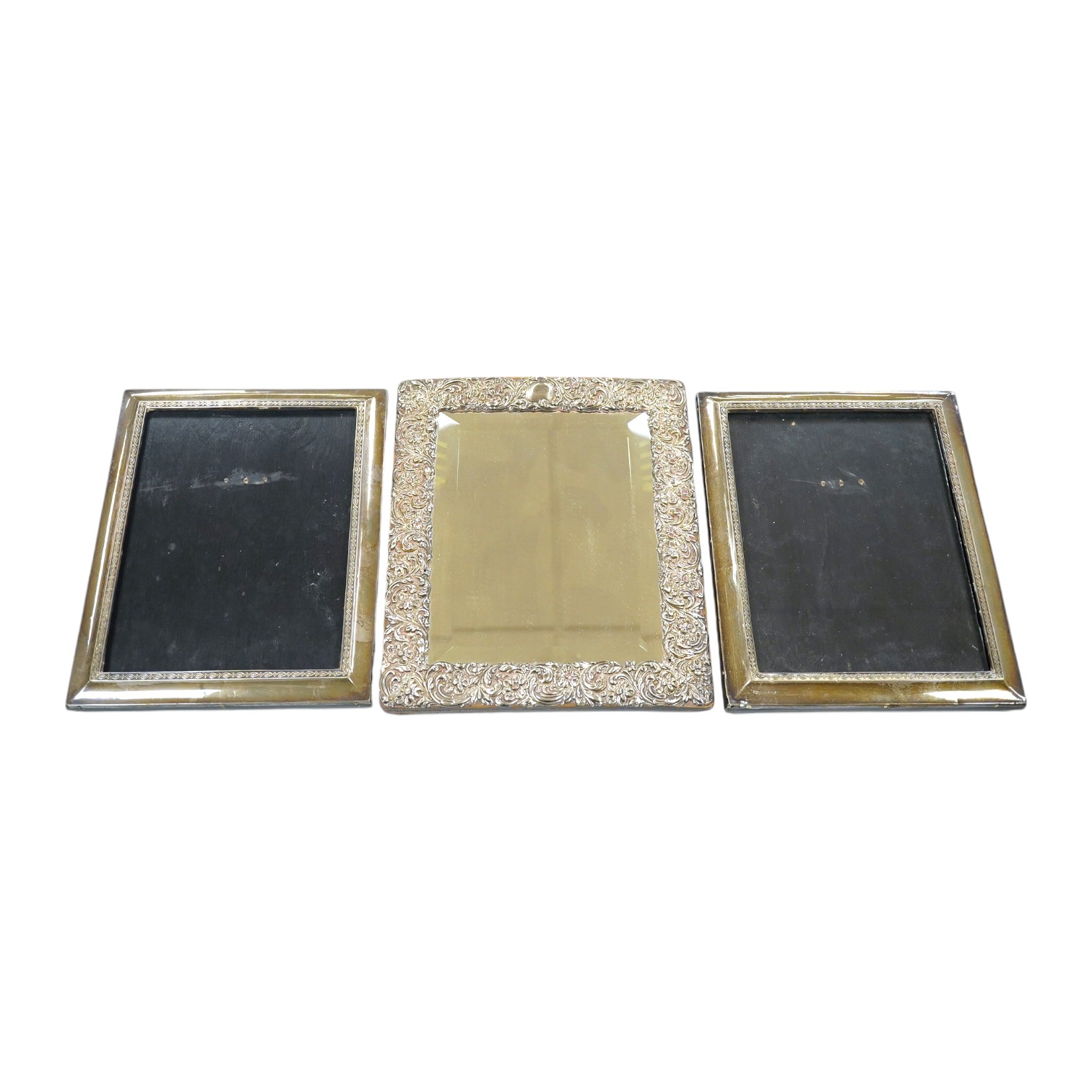 A late Victorian repousse silver mounted rectangular easel mirror, Birmingham, 1900, 26.8cm, together with a pair of George V silver mounted rectangular photograph frames, Birmingham, 1917. Condition - poor